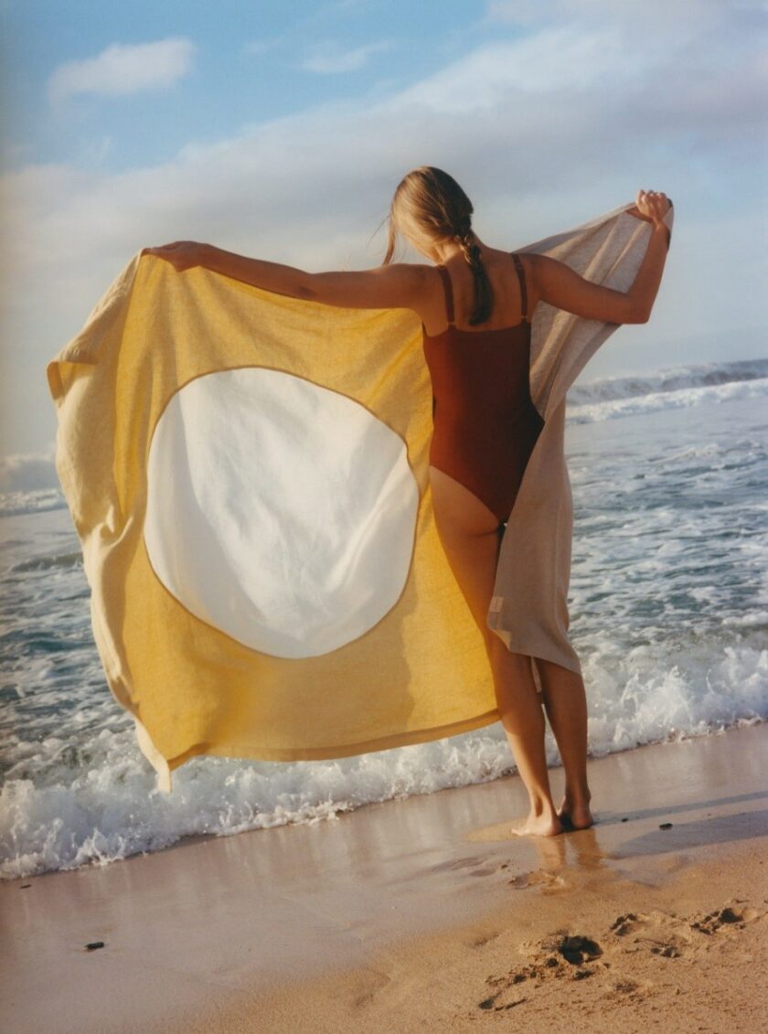 Ręcznik plażowy w kolorach naturalnego beżowo-szarego lnu, bieli i żółtego wykonany z lnu. U dołu prostokąt z naturalnym lnem, u góry żółty z naszytym kształtem koła w białym kolorze.
