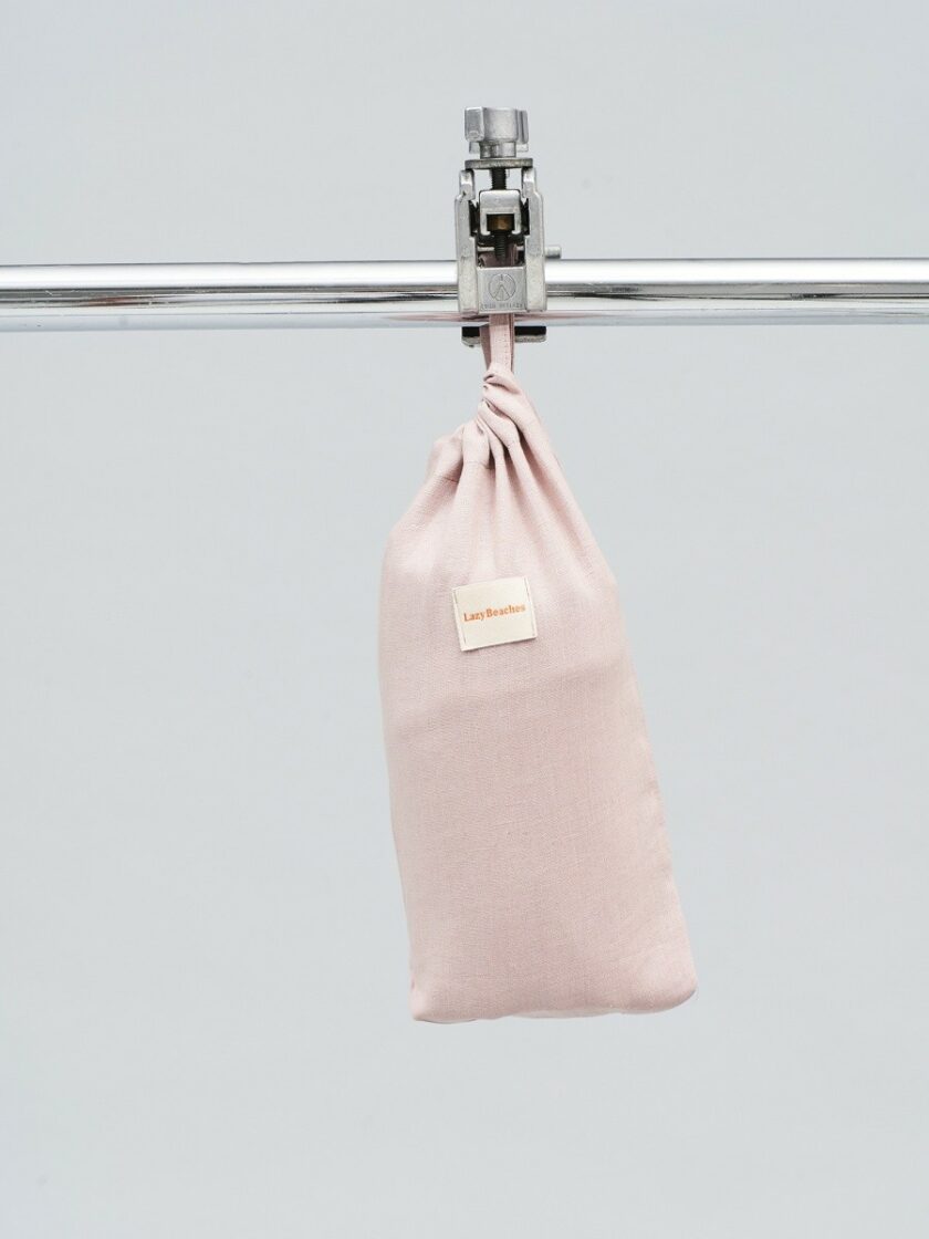 Lniany woreczek w kolorze pudrowego różu z naszywką z logo marki do pakowania ręcznika plażowego.